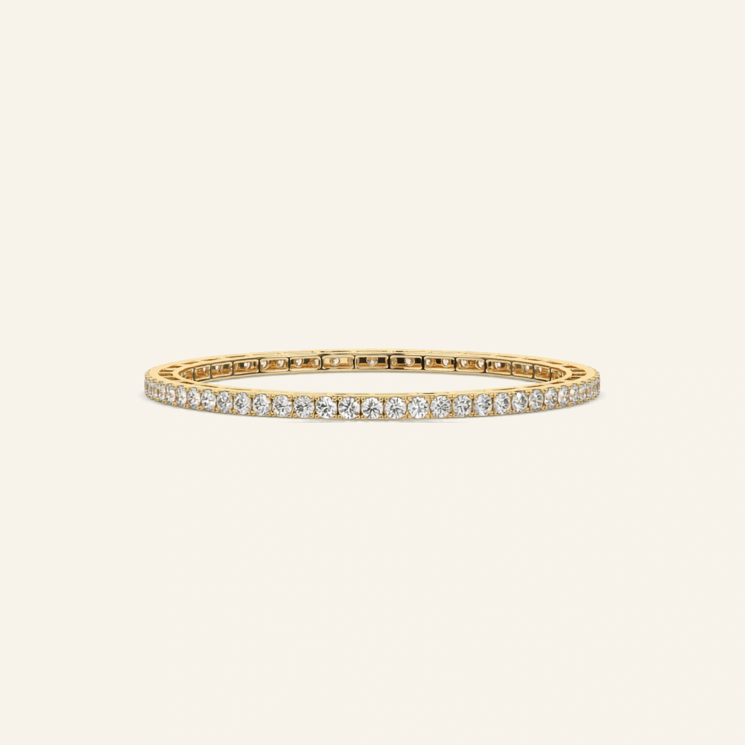 A yellow gold bangle bracelet featuring a continuous row of small clear stones along one side, displayed on a light cream background.