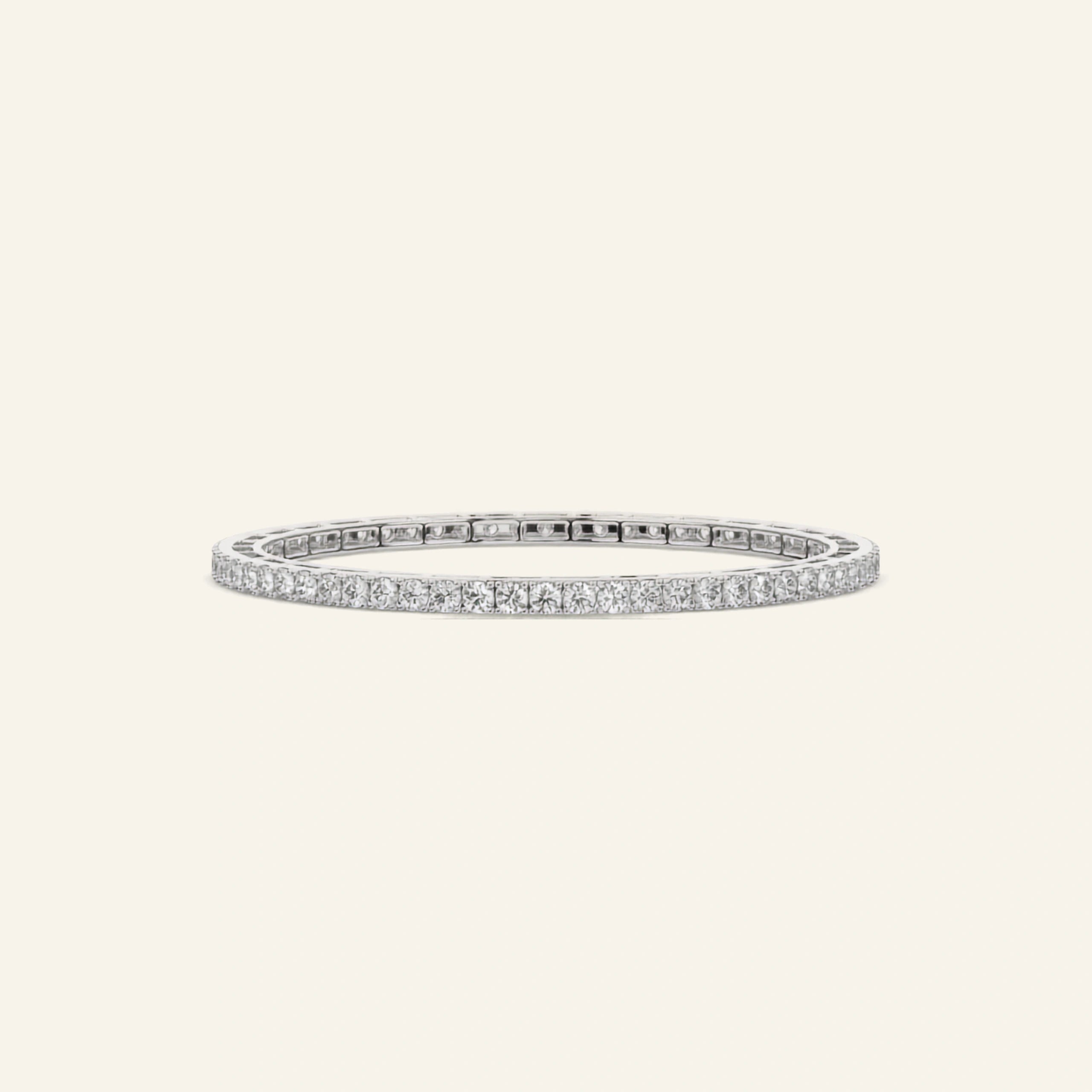 A white gold bangle bracelet featuring a continuous row of small clear stones along one side, displayed on a light cream background.