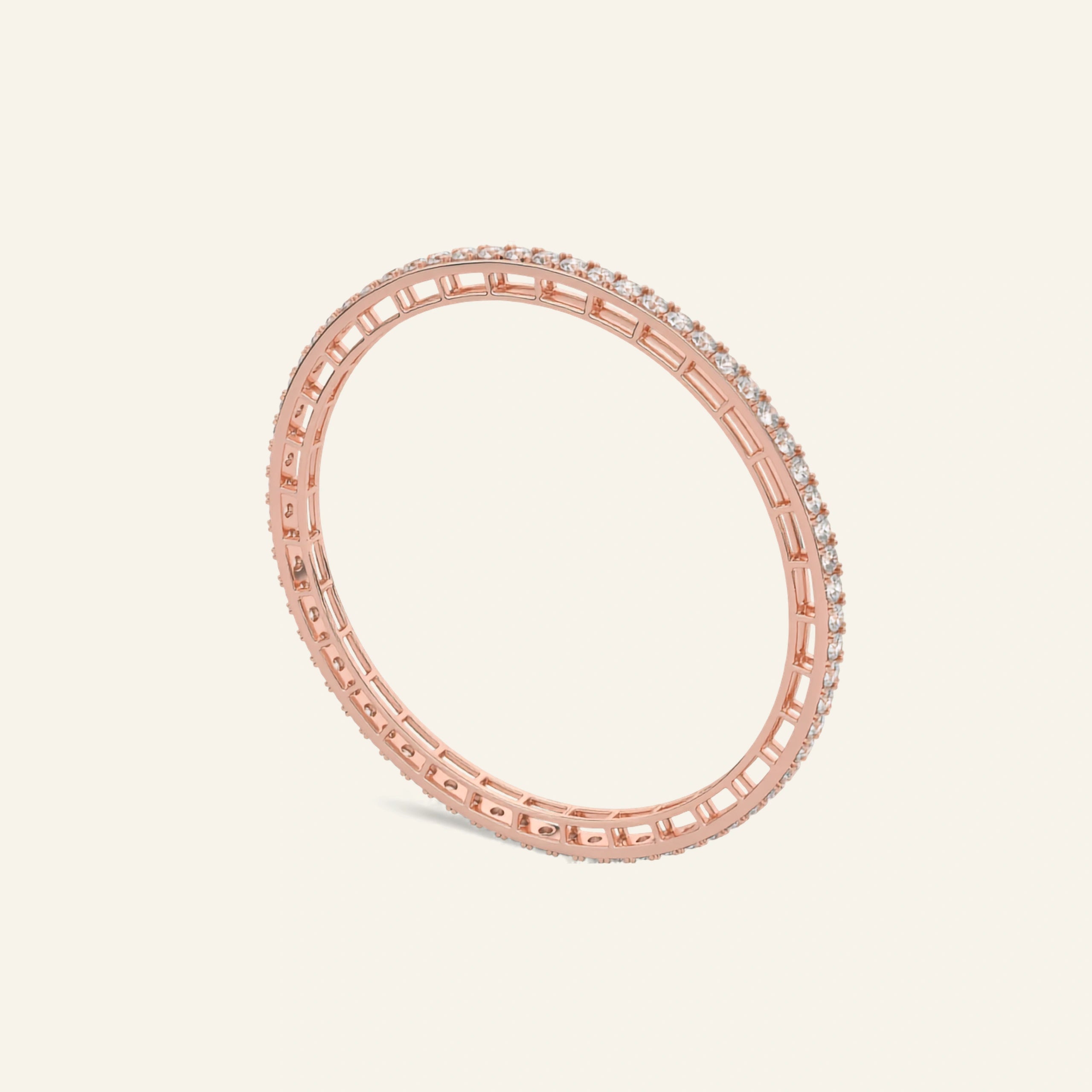 A rose gold eternity bangle bracelet with a continuous line of small clear stones, shown on a light cream background.